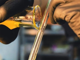 A close-up of a person wearing gloves pouring yellow liquid into a glass