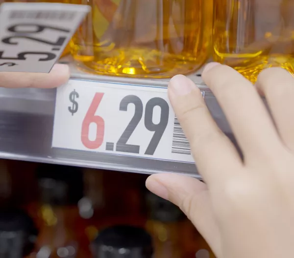 Closeup of grocery store worker increasing prices on cooking oil from $5.29 to $6.29. Rising food costs concept.