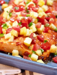 large piece of salmon covered in pineapple and tomato salsa on a pan