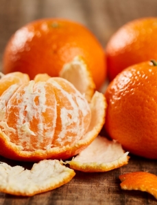 Seasonal produce - four clementine citrus fruits on a wooden board, one peeled