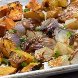 chopped winter vegetables sprinkled with sesame seeds and scallions roasted on baking sheet