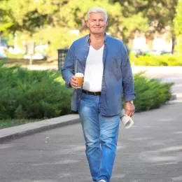 older man walking down street with coffee and paper