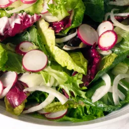 close up on bowl of salad with mixed greens and radish slices