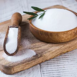 bowl and scoop filled with sugar on wood cutting board