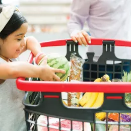 Young girl placing produce into a shopping cart