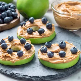 Plate with green apple slices covered in peanut butter and sprinkled with blueberries