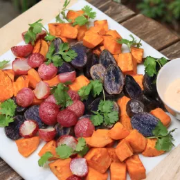 white platter filled with colorful root vegetables and side bowl of creamy sauce