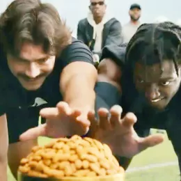 2 men reaching towards a pile of almonds in the foreground