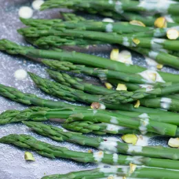 cooked asparagus covered in sauce and pistachios