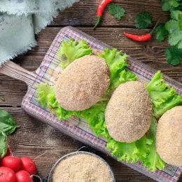 frozen Kiev cutlets lie on a wooden board covered with a thin kitchen towel. Raw frozen breaded stuffed chicken