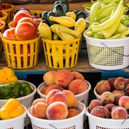 Seasonal produce - baskets of tomatoes, squash, peppers, peaches and other fruit and vegetables for sale in July