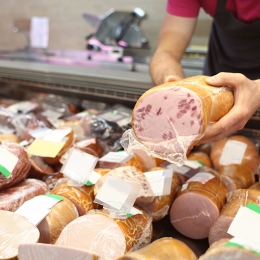 Male seller holding piece of deli meat in butcher shop