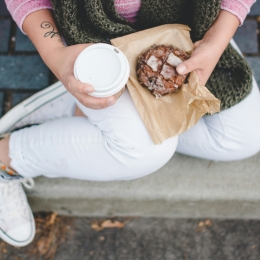 A person holding a coffee drink and a glazed pastry