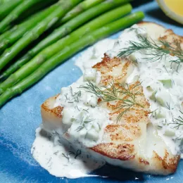 piece of white fish covered in tartar sauce with some asparagus on a plate