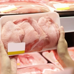 person holding a package or raw chicken in front chicken shelf at supermarket