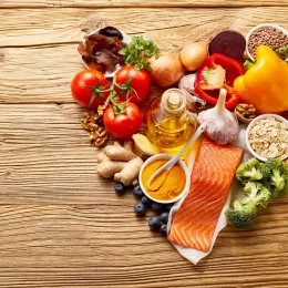 A collection of food in the shape of a heart including raw salmon, olive oil, ginger, nuts, berries, oats, beans, and assorted fruits and vegetables.