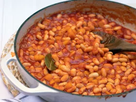 large ceramic sauce pan filled with beans and sauce with wooden spoon.