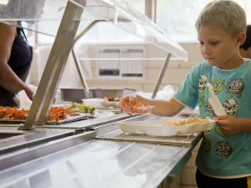 A boy in the school cafeteria adding foods his lunch tray