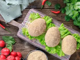 frozen Kiev cutlets lie on a wooden board covered with a thin kitchen towel. Raw frozen breaded stuffed chicken