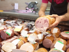 Male seller holding piece of deli meat in butcher shop