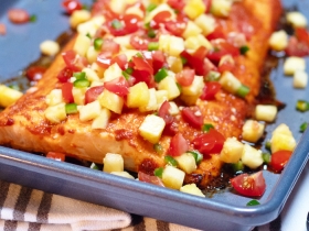 large piece of salmon covered in pineapple and tomato salsa on a pan