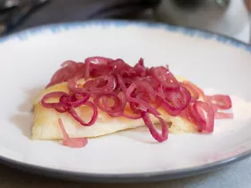 tilapia on a plate covered in cooked red onions