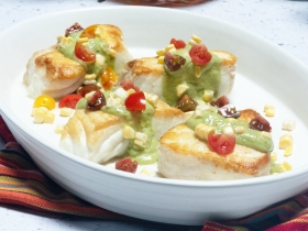 white bowl with fish covered in green sauce and other vegetables