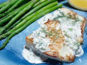 piece of white fish covered in tartar sauce with some asparagus on a plate