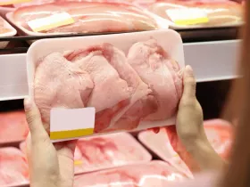 person holding a package or raw chicken in front chicken shelf at supermarket