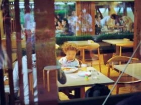 Looking through a restaurant window at a young child sitting at a table with a meal in front of him