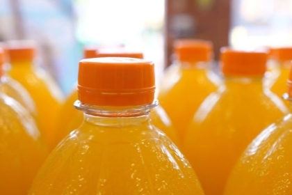 Close up of top parts of orange soda in plastic bottles on a display in a supermarket