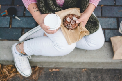 A person holding a coffee drink and a glazed pastry