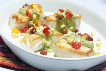 white bowl with fish covered in green sauce and other vegetables