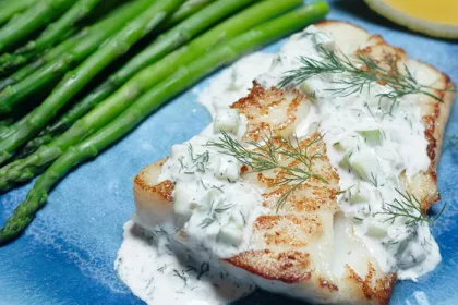 piece of white fish covered in tartar sauce with some asparagus on a plate