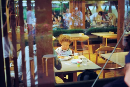 Looking through a restaurant window at a young child sitting at a table with a meal in front of him