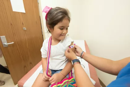 A young girl smiles as a nurse puts a colorful bandage on her arm after administering a vaccine.