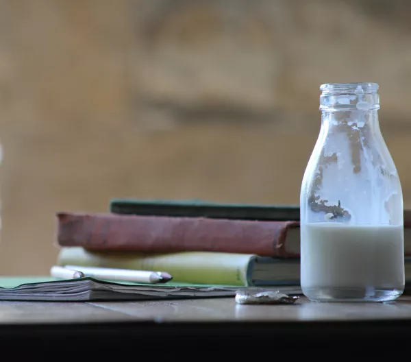 Half full container of plain milk next to books and pencils