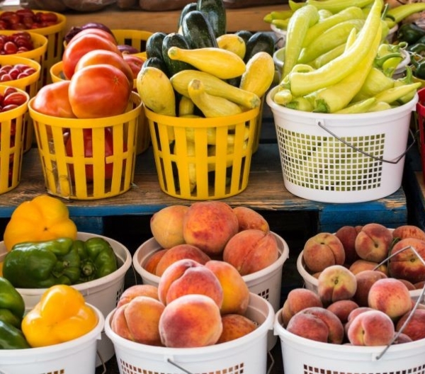 Seasonal produce - baskets of tomatoes, squash, peppers, peaches and other fruit and vegetables for sale in July