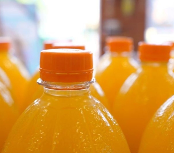 Close up of top parts of orange soda in plastic bottles on a display in a supermarket