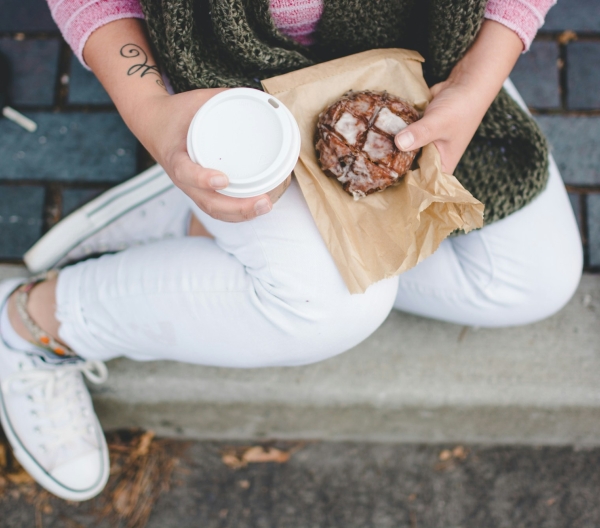 A person holding a coffee drink and a glazed pastry