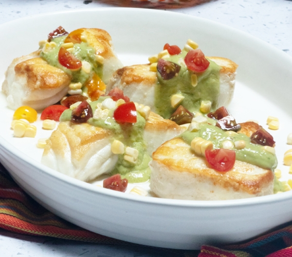 white bowl with fish covered in green sauce and other vegetables