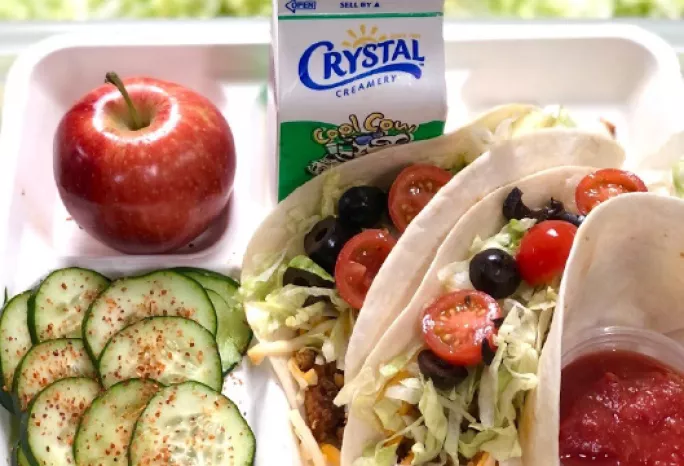 A lunch tray: tofu tacos, cucumber salad, an apple, and milk.