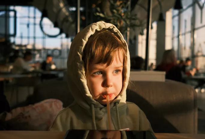 A closeup of a young child wearing a hoodie and drinking from a straw in a restaurant