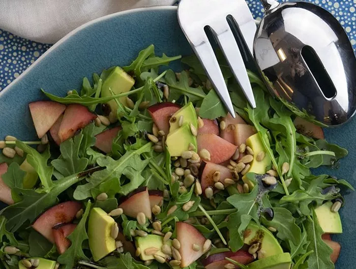 salad with greens, nectarine, avocado, sunflower seeds in blue bowl.