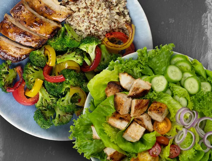 plate of chicken, vegetables, and quinoa alongside plate of chicken salad