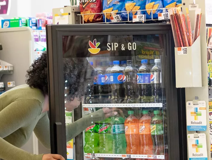 woman reaching into a soda cooler at checkout