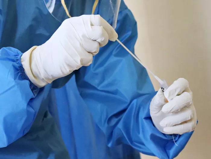 A person in a protective medical suit and gloves inserting a cotton swab into a tube