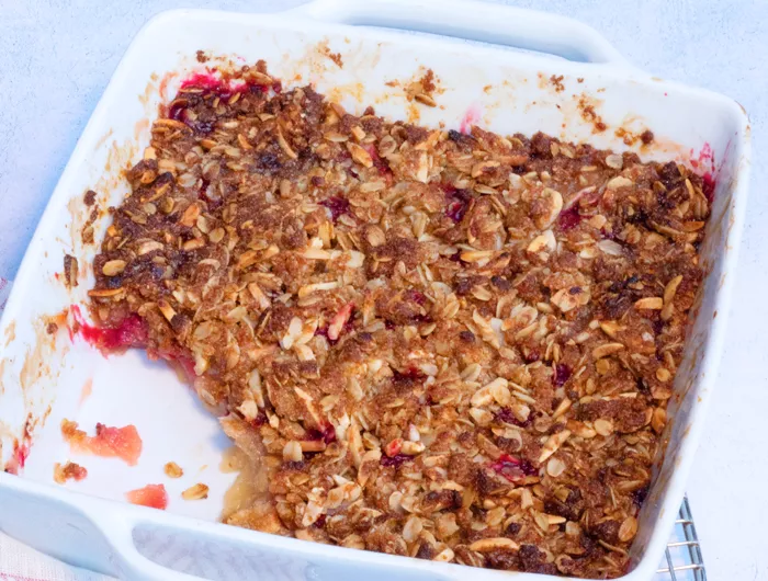 White serving dish with apple raspberry almond crisp, missing a spoonful in the corner of dish.