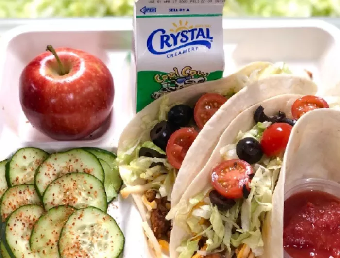 A lunch tray: tofu tacos, cucumber salad, an apple, and milk.