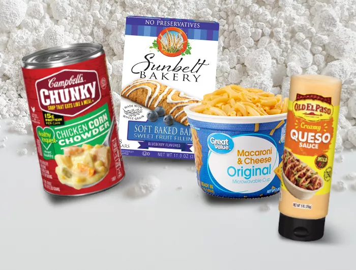 Canned soup, boxed mac & cheese, breakfast bars, and queso--packaged foods containing titanium dioxide--against a background of the powdered white substance.